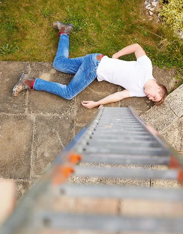 Un homme est tombé d'une échelle et est allongé par terre dans un jardin, illustrant un accident domestique.