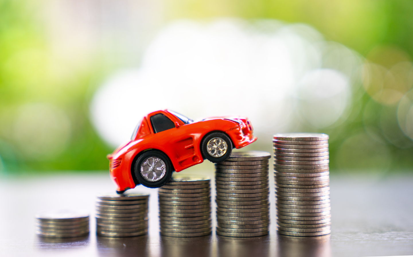 Une petite voiture rouge est posée sur des piles de pièces de monnaie, symbolisant les coûts croissants de l'assurance auto.