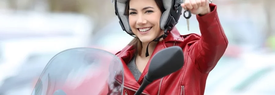 Jeune femme souriante en veste rouge et casque de moto, tenant les clés de son scooter en main