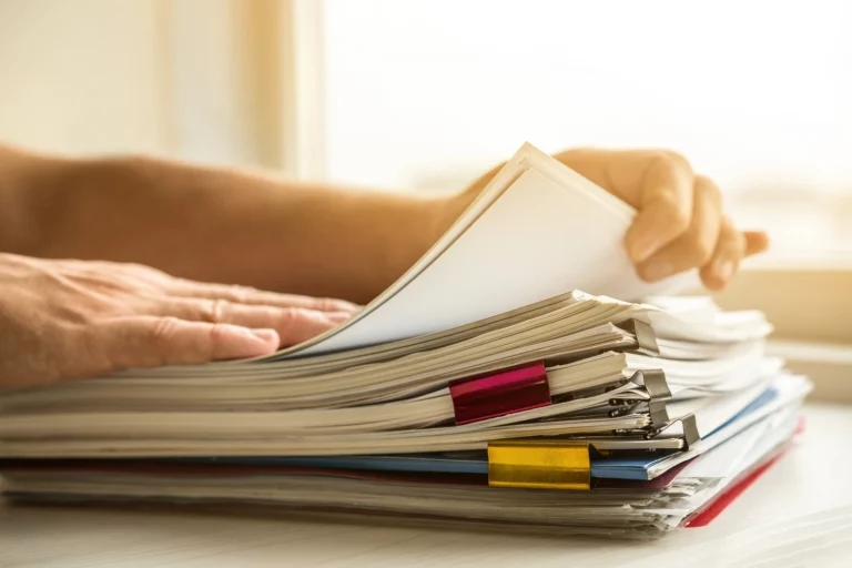 Une personne feuillette une pile de dossiers attachés avec des trombones colorés, symbolisant la gestion et l'organisation des documents importants liés à l'assurance habitation