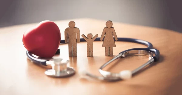 Une image symbolique représentant la santé familiale. On y voit des silhouettes en bois d'une famille (père, mère, enfant) entourées d'un stéthoscope et d'un cœur rouge. Cette illustration évoque la protection offerte par une mutuelle santé