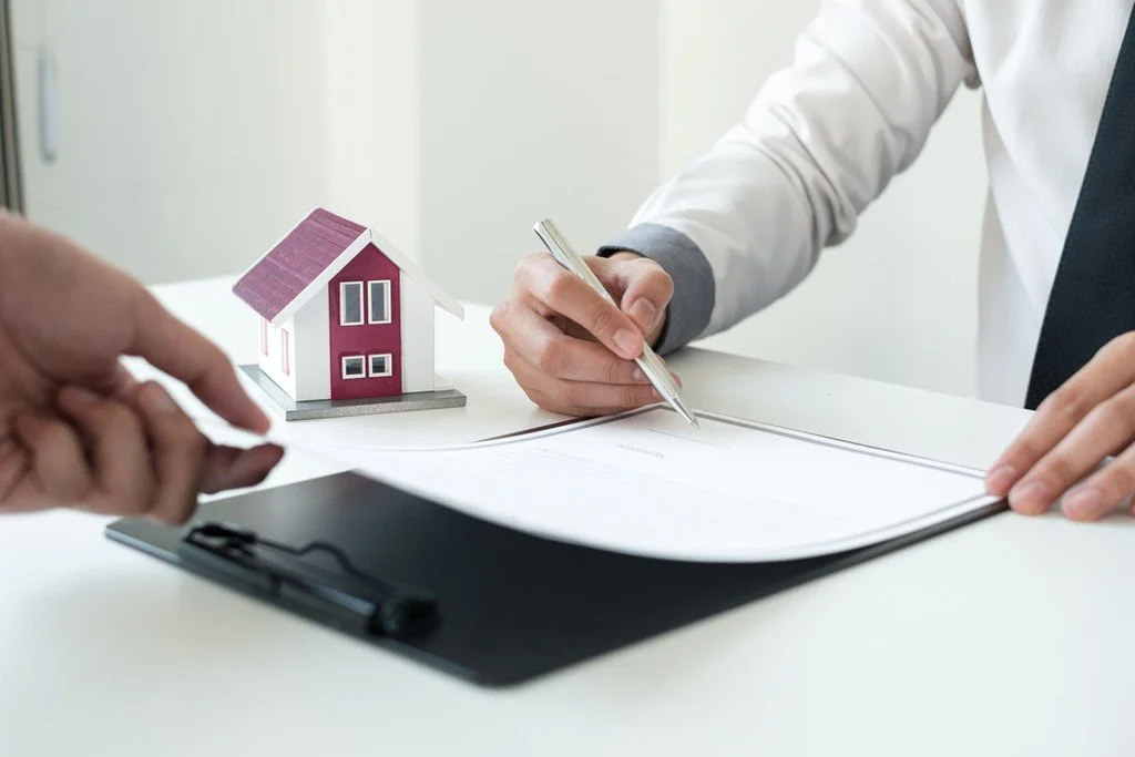 Personne résiliant un contrat d'assurance habitation, avec une maquette de maison en arrière-plan.