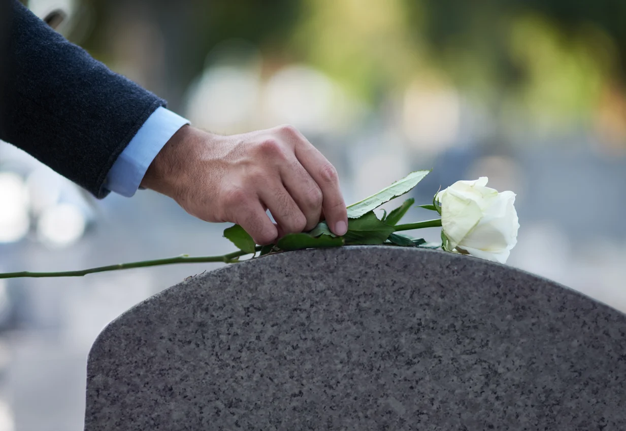 Main posant une rose blanche sur une pierre tombale, symbolisant le respect et le recueillement lors des funérailles