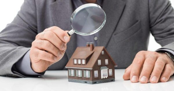 Un homme en costume examine une petite maquette de maison à l'aide d'une loupe, symbolisant le processus de contre-expertise en assurance habitation.