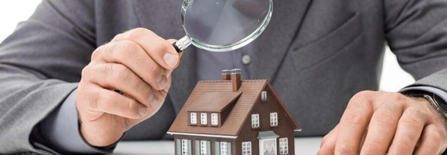 Un homme en costume examine une petite maquette de maison à l'aide d'une loupe, symbolisant le processus de contre-expertise en assurance habitation.