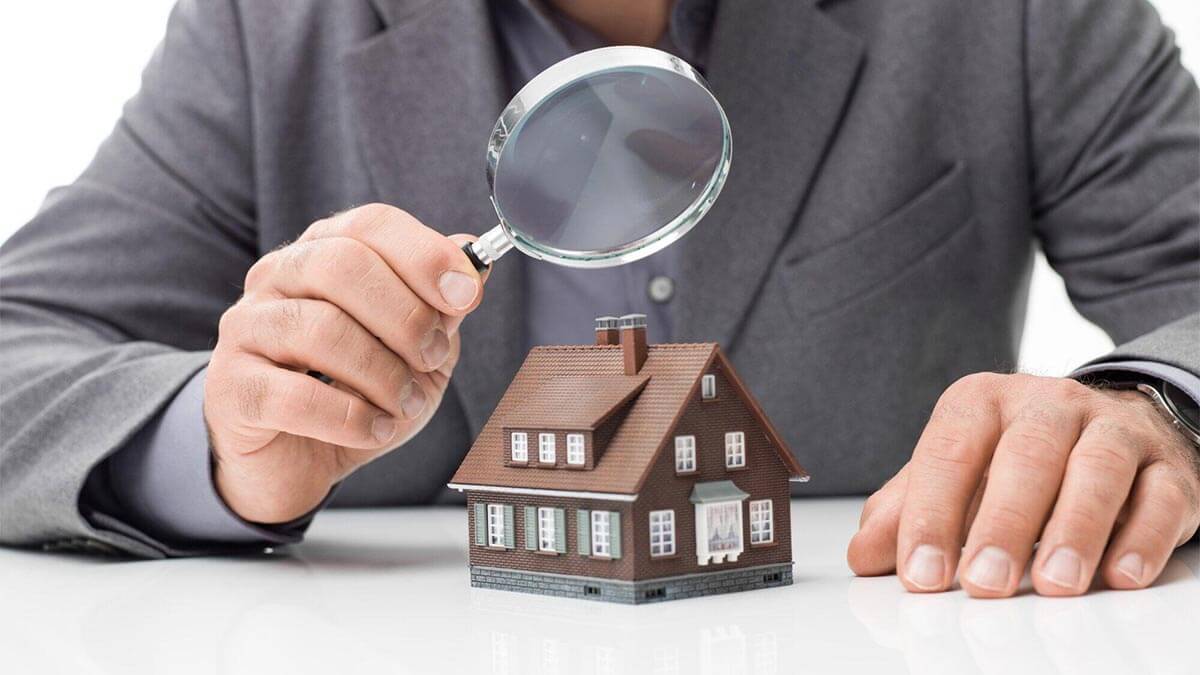 Un homme en costume examine une petite maquette de maison à l'aide d'une loupe, symbolisant le processus de contre-expertise en assurance habitation.