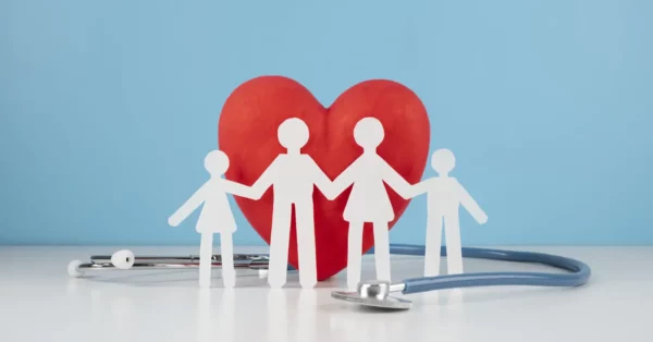 une famille (quatre silhouettes) devant un cœur rouge, entourée d'un stéthoscope. Cette image symbolise la protection de la santé à travers une mutuelle ou une complémentaire santé