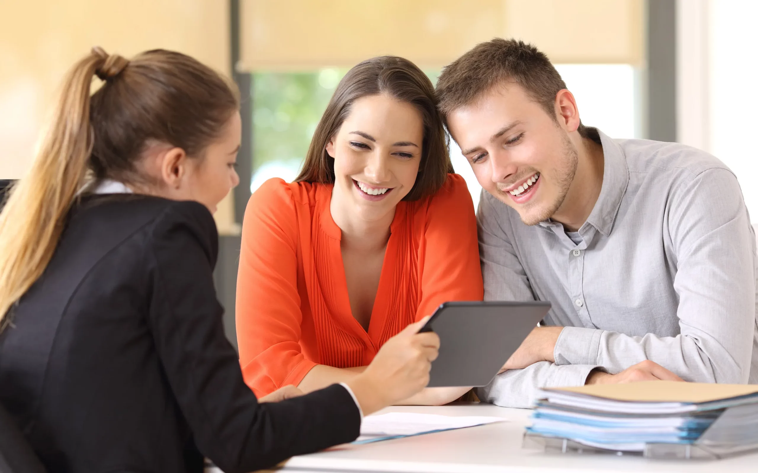 Une conseillère en assurance montre des informations sur une tablette à un couple souriant. Cette image représente un rendez-vous de conseil pour choisir ou cumuler une mutuelle et une complémentaire santé