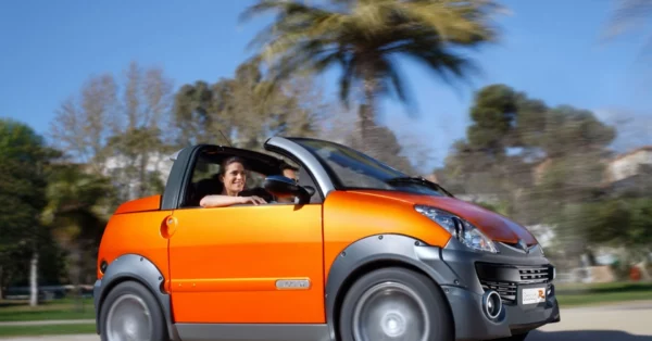 Voiturette orange en pleine conduite, avec une conductrice souriante, sous un ciel bleu et des palmiers en arrière-plan