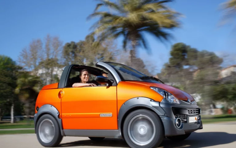 Voiturette orange en pleine conduite, avec une conductrice souriante, sous un ciel bleu et des palmiers en arrière-plan