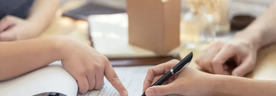 Des personnes examinent et signent un contrat d'assurance emprunteur, symbolisant une discussion sur le changement d'assurance pour un prêt immobilier, avec une petite maquette de maison en arrière-plan