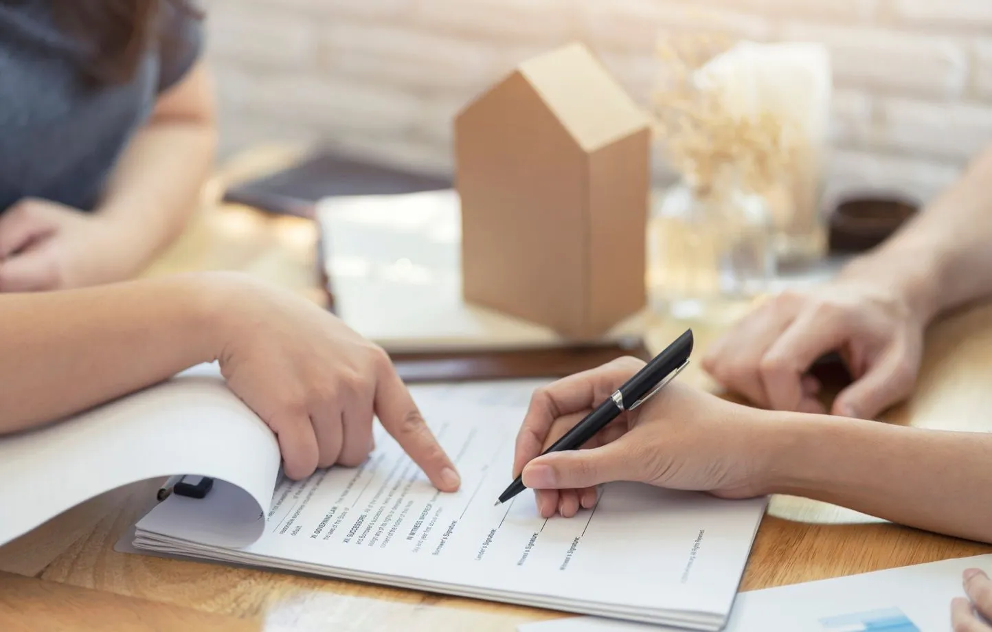 Des personnes examinent et signent un contrat d'assurance emprunteur, symbolisant une discussion sur le changement d'assurance pour un prêt immobilier, avec une petite maquette de maison en arrière-plan