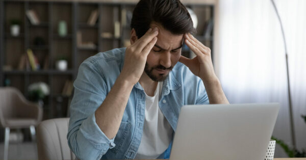 Homme stressé cherchant des informations sur l'ordinateur, tenant sa tête entre ses mains dans un moment de frustration.