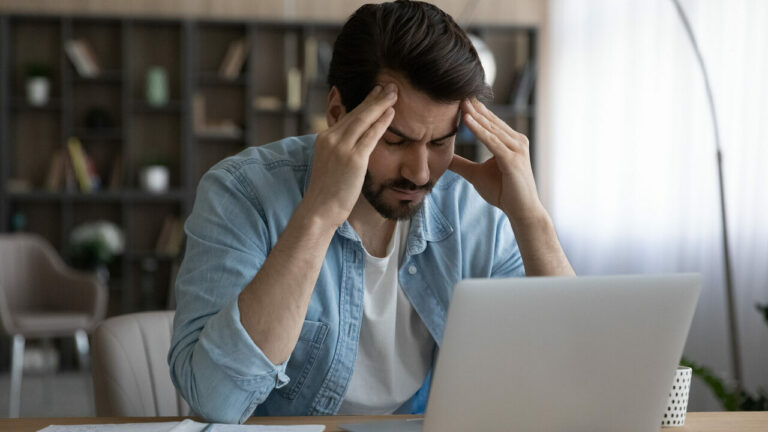 Homme stressé cherchant des informations sur l'ordinateur, tenant sa tête entre ses mains dans un moment de frustration.