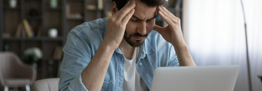 Homme stressé cherchant des informations sur l'ordinateur, tenant sa tête entre ses mains dans un moment de frustration.